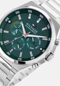 Montre à cadran vert avec bracelet en acier inoxydable argenté, présentant de grands index horaires, des affichages de la date et du jour, ainsi qu'une fonction chronographe.