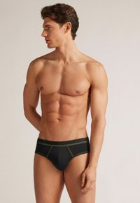 Svarta bomullsbriefs med olivgrön kontrasterande kant, med en bekväm midjeresår och en åtsittande passform, visade på en manlig modell.