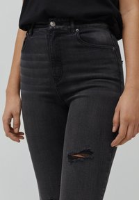 Mustat korkeavyötäröiset farkut, joissa kulutettu ilme näkyvine repaleineen, viisi taskua ja napillinen suljenta.