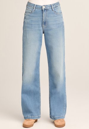 Hellblaue, hoch taillierte Jeans mit weitem Bein, Vordertaschen und Knopfverschluss, getragen mit beigen Wildlederschuhen.