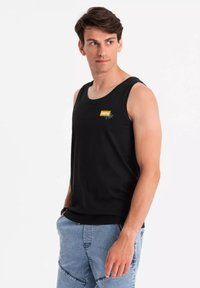 Svart ärmlös linne med rund halsringning, prytt med en färgglad grafik med texten "Summer Vibe" på framsidan. Bärs med ljusblå denimshorts.