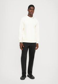 White sweatshirt with ribbed cuffs and hem, featuring a small logo on the collar. Paired with black pants and black sneakers.