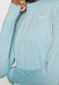 Helle blaues, langärmeliges Sportshirt mit geripptem Muster und kleinem weißen Nike-Logo auf der Brust, entworfen für Komfort und Leistung.