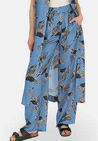 Niebieskie spodnie w wzory z czarnymi liśćmi, charakteryzujące się luźnym krojem, elastycznym pasem i bocznymi kieszeniami. Gładka tekstura tkaniny.