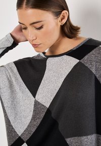 Grijze en zwarte pullover met een groot geometrisch patroon, gemaakt van zachte stof, voorzien van een ronde halslijn en losse mouwen.
