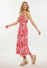 Vestido maxi floreado en rojo y blanco con lados recortados, tirantes finos y una falda fluida, combinado con sandalias de cuña atadas en beige.