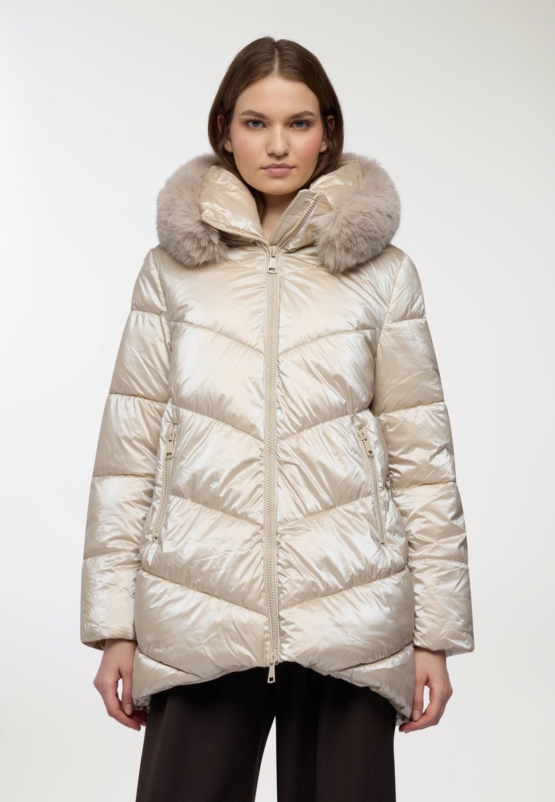 Giacca a vento beige lucida con motivo a chevron, dotata di cappuccio rifinito in pelliccia sintetica e tasche anteriori con zip. Tessuto liscio e taglio fino al ginocchio.