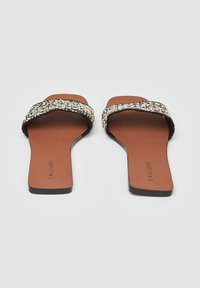 Sandali piatti intrecciati neri e beige con design a strap incrociato, soletta marrone e suola nera liscia. Logo del brand "CALLIOPE" sulla soletta.