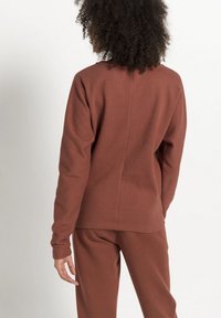 Pull en maille texturée marron avec des manches longues, comportant un col rond et une couture dans le dos.