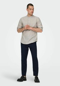 Camicia grigia chiaro con maniche arrotolate, abbinata a pantaloni navy slim-fit e scarpe nere stringate. Tessuto morbido, vestibilità casual.