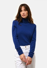 Królewsko-niebieski sweter z golfem o miękkiej fakturze, z długimi rękawami i luźnym krojem, zestawiony z białymi spodniami o wysokim stanie.