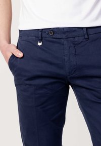 Pantaloni blu navy in tessuto liscio con chiusura a bottoni, passanti per cintura e tasche laterali, che presentano una vestibilità su misura.