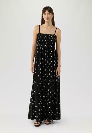 Robe maxi noire avec un motif abstrait blanc, présentant des bretelles fines, un bodice smocké et une silhouette fluide. Texture satinée.