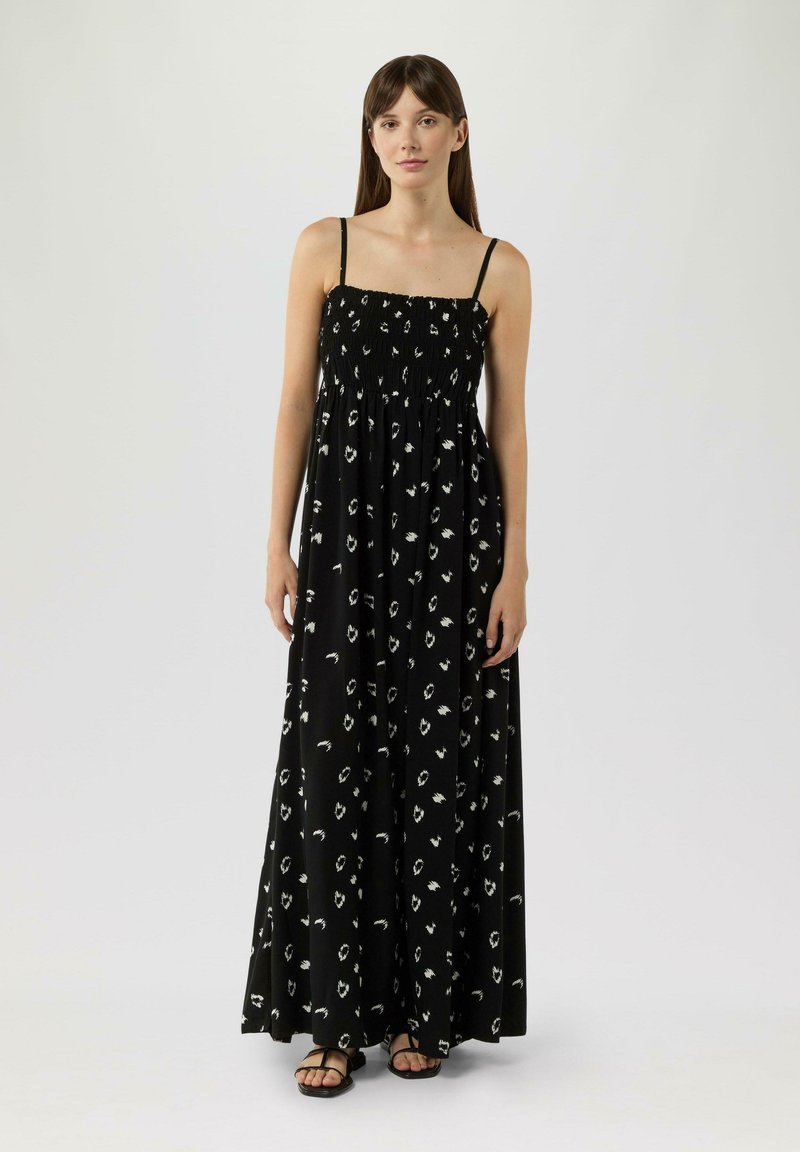Zwarte maxi-jurk met wit abstract patroon, met dunne bandjes, gerimpelde taille en een vloeiende silhouet. Satijnen textuur.