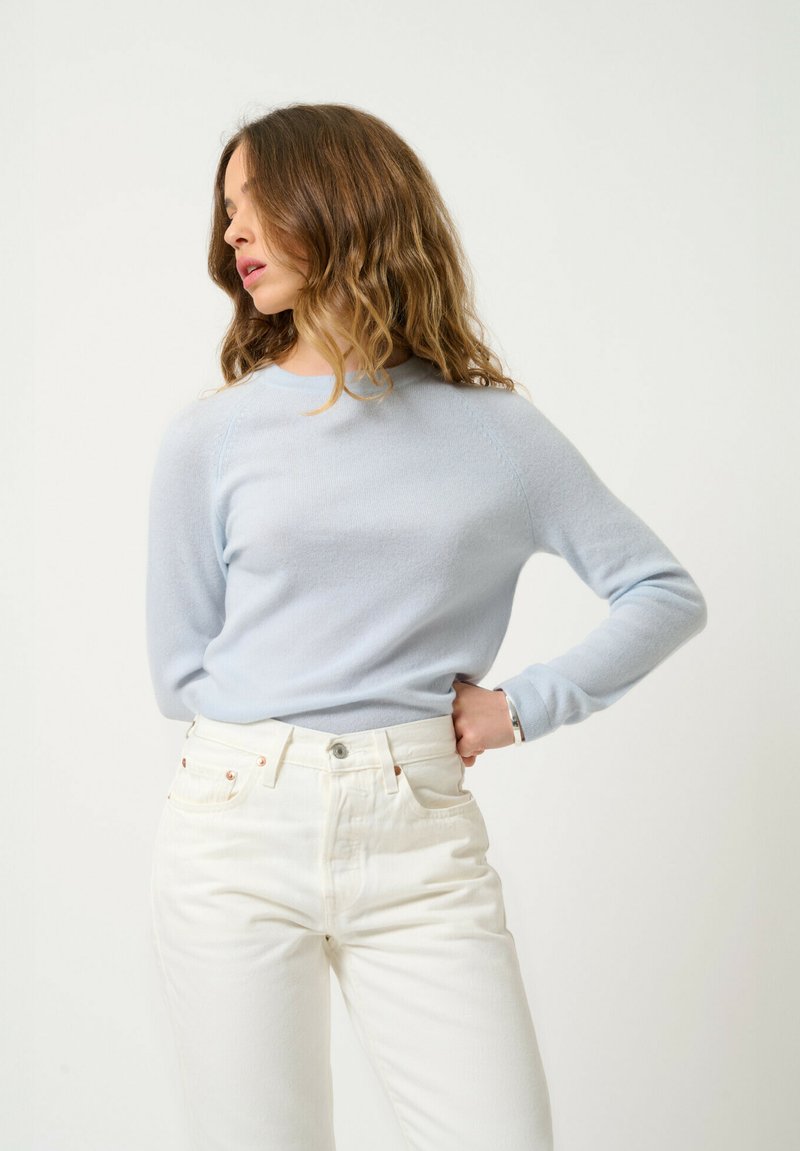 Ljust blå stickad tröja med långa ärmar, rund halsringning och ribbade kanter, tillsammans med vita jeans med metallknappdetaljer.