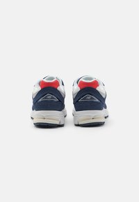 Paire de baskets athlétiques bleu marine, blanches et rouges vues de dos, avec semelles rembourrées et logo New Balance sur les talons.