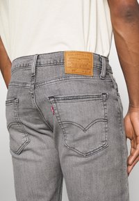 Grijze Levi's 512 jeans met een gestructureerd oppervlak, subtiele vervaging, twee achterzakken en een tan leren taillebandlabel met merkdetails.