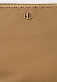 Pochette en nylon beige avec une finition texturée et un accent doré "R.L.". Elle dispose d'une fermeture éclair sur le bord supérieur pour un stockage sécurisé.