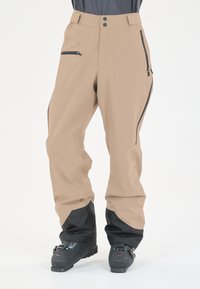 Beige Outdoor-Hosen mit schwarzen unteren Bündchen, zwei Reißverschlusstaschen, einer glatten Textur und einer lockeren Passform, die für Beweglichkeit konzipiert ist.