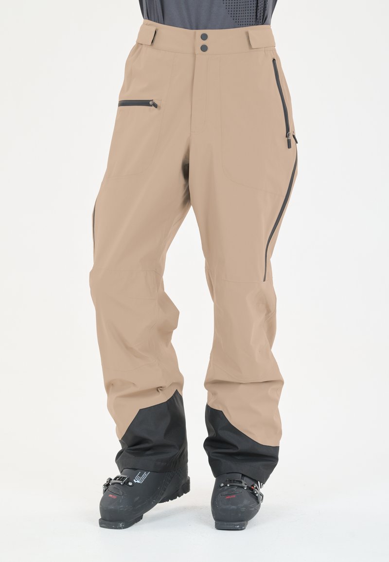 Beige Outdoor-Hosen mit schwarzen unteren Bündchen, zwei Reißverschlusstaschen, einer glatten Textur und einer lockeren Passform, die für Beweglichkeit konzipiert ist.
