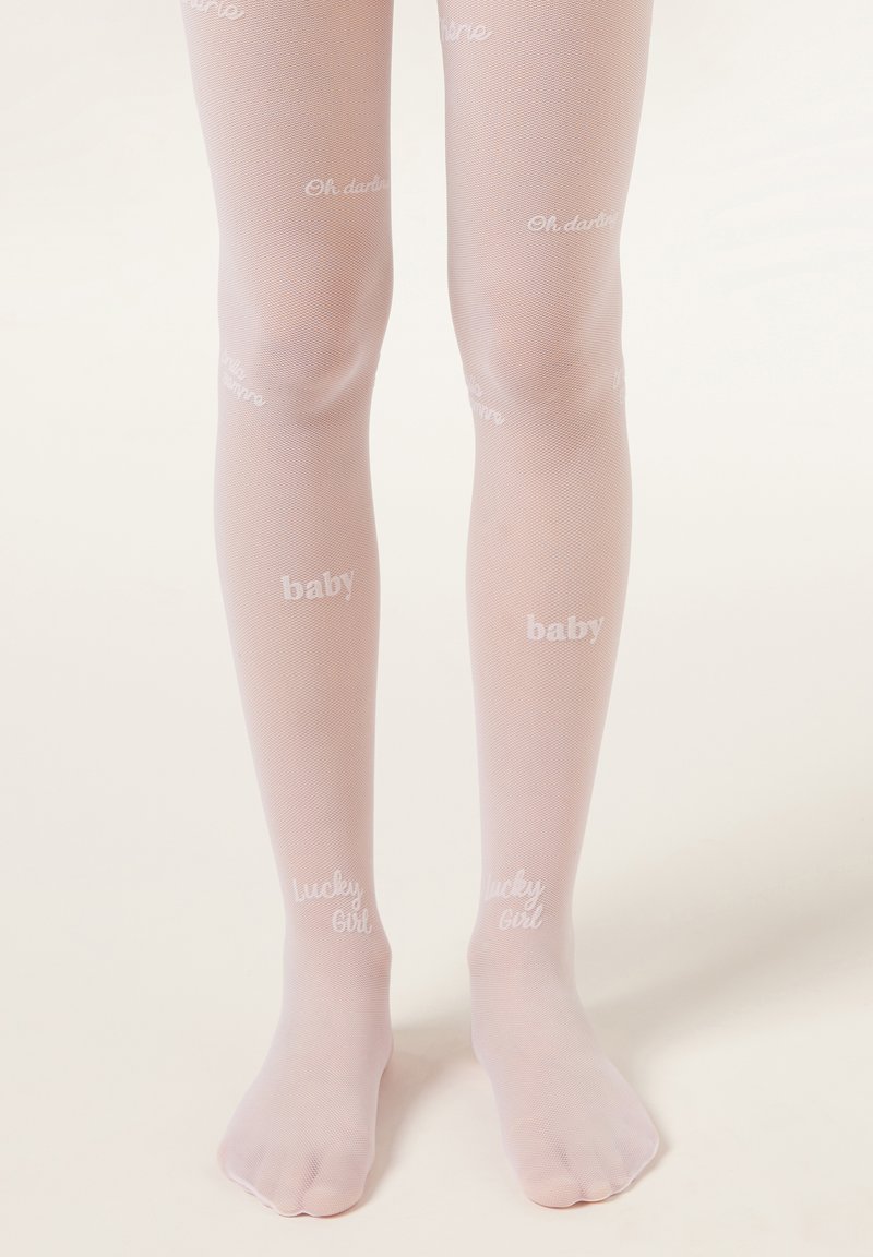 Jambes d'enfant portant des collants rose clair avec les mots blancs « baby » et « lucky girl » imprimés dessus, debout sur un fond uni clair.