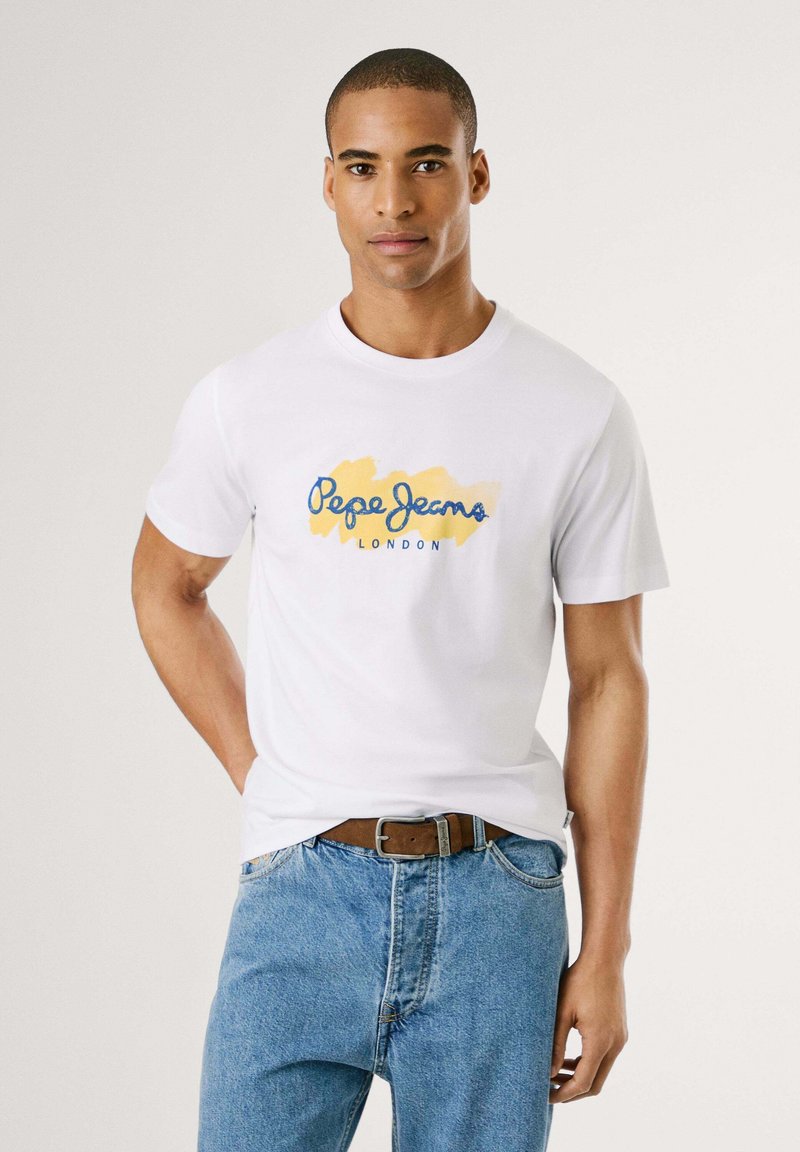 Balti medvilninis marškinėliai su mėlyna ir geltona logotipo dizainu "Pepe Jeans London." Apvalus kaklas, trumpomis rankovėmis, derinami su mėlynomis džinsinėmis kelnėmis.