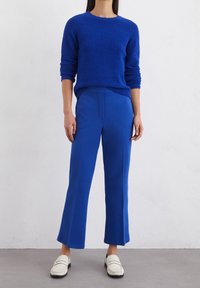 Blauwe gestructureerde trui met lange mouwen, gecombineerd met hoge blauwe wijde broek en witte instappers. Subtiele naaddetails op de broek.