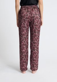 Różowe spodnie w kwiatowy wzór z elastycznym pasem, luźnym krojem i gładką teksturą, z ciemnoczerwonymi i czarnymi wzorami kwiatów.