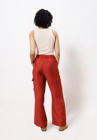 Rode wijde broek met een gestructureerde afwerking, voorzien van een elastische tailleband en zijkant cargozakken. Gecombineerd met een beige geribbelde tanktop.