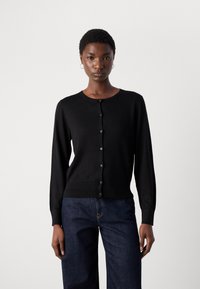 Svart cardigan med lange ermer, rund hals og knappelukking foran. Har ribbestrikket kant og mansjetter, laget av myk strikket stoff.