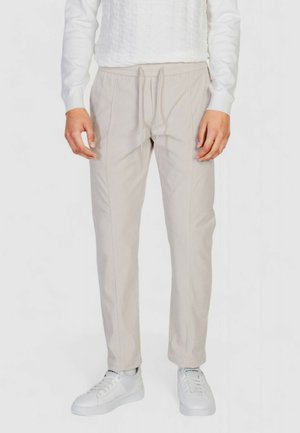 Pantaloni beige a coste con vita elastica e cordino. Abbinati a sneakers bianche. Vista frontale, design aderente.