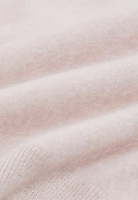 Tessuto di lana rosa chiaro con una texture liscia e una leggera lucentezza, caratterizzato da un bordo a coste e una leggera peluria.