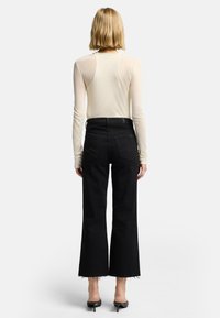 Jeans neri a gamba larga con orli sfrangiati, vita alta e due tasche posteriori. Abbinati a una maglietta a maniche lunghe color crema.