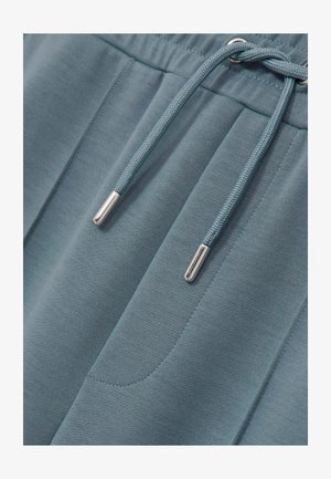 Ljusblå joggerbyxor gjorda av mjukt material med dragsko i midjan som har silverfärgade detaljer och två sidofickor.