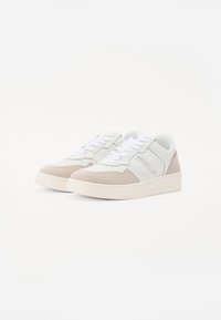 Sneaker in pelle bianca e suede beige chiaro con punte arrotondate, lacci bianchi e dettagli testurizzati ai lati e sulla linguetta.