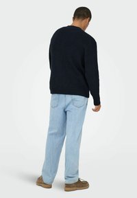 Marineblauer gerippter Strickpullover mit langen Ärmeln, kombiniert mit hellblauen, weit geschnittenen Jeans und braunen Freizeitschuhen, von hinten betrachtet.