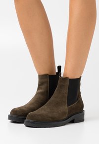 Ruske nubuk ankle bootsit, joissa on elastiset sivupaneelit ja teksturoitu musta pohja. Varressa on vetoketju, joka helpottaa pukemista.