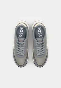 Baskets grises avec un matériau texturé, design à lacets, logo "BOSS" bien en vue sur les semelles intérieures, accents crème et semelle en caoutchouc.