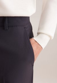 Granatowe spodnie charakteryzują się gładkim materiałem, dopasowanym krojem i kieszeniami po bokach. Na górze widoczny jest biały sweter z prążkowanymi mankietami.