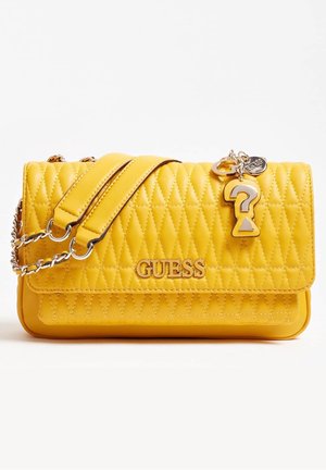 Sac à main matelassé jaune avec une bandoulière en chaîne, doté d'un plaquette de logo et d'un pendentif en forme de point d'interrogation. Texture lisse et forme structurée.