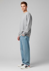 Felpa grigia chiara con colletto a giro, spalle scese, abbinata a jeans azzurri a vestibilità ampia e sneakers bianche con dettagli neri e rossi.