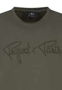 T-shirt vert olive avec un col rond, présentant un texte brodé en relief "Project x Paris" dans une police cursive.