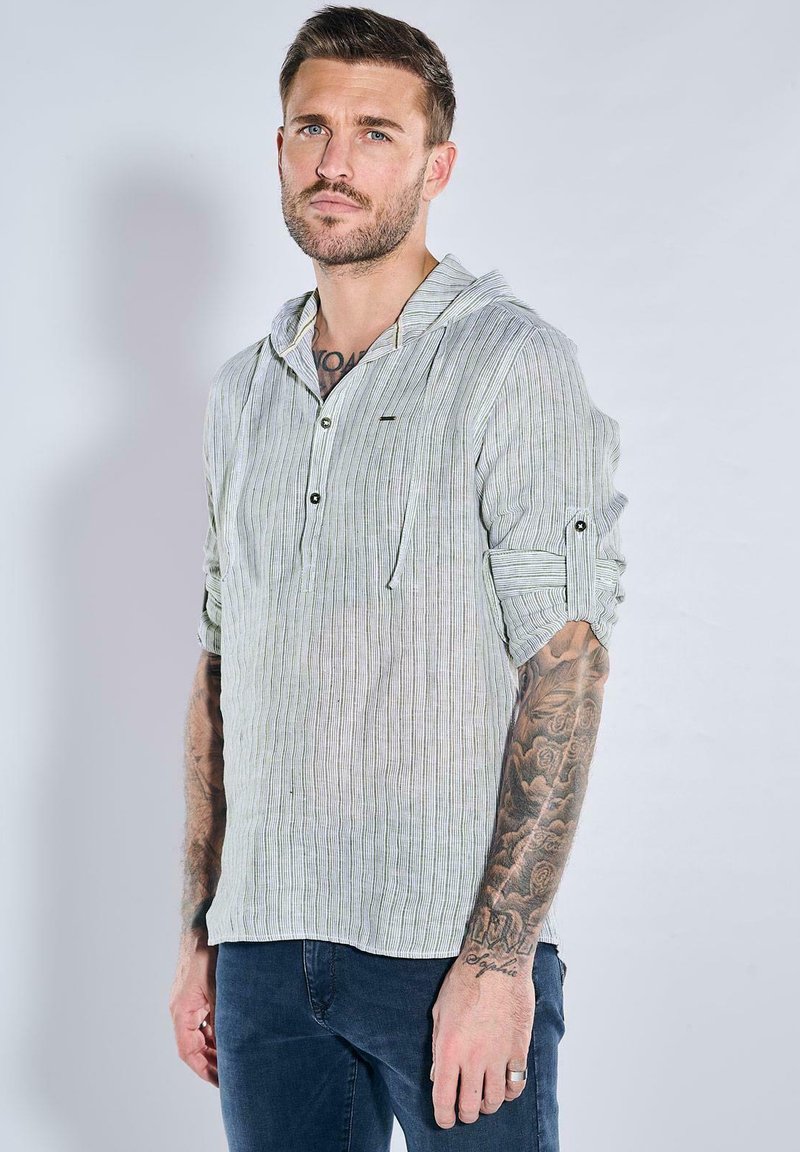 Leichte, gestreifte Langarmbluse in Weiß und Grün mit Kapuze, knöpfbarem Vorderteil und hochgekrempelten Ärmeln. Jeans sind darunter sichtbar.