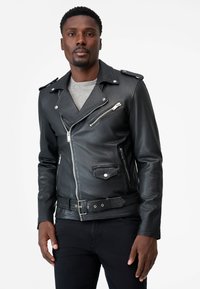 Zwarte leren motorjack met epauletten, zilveren ritsen, een ceintuur in de taille en een gestructureerde afwerking; bovenop een grijs shirt.