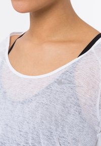 White, lightweight athletic top with a loose fit, featuring a round neckline and a small silver Nike logo on the chest.