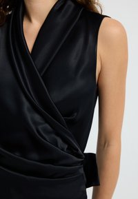 Top negro sin mangas hecho de una tela suave, con un diseño envolvente que presenta detalles drapeados y un adorno atado en la cintura.