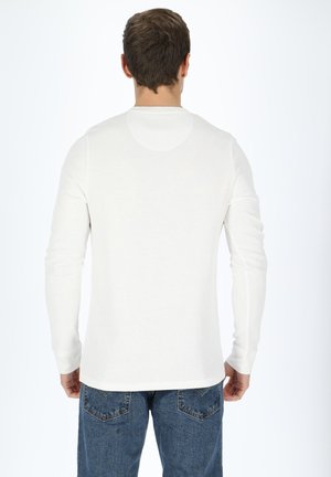 Langärmliges weißes Hemd aus weichem, geripptem Stoff, mit rundem Halsausschnitt und geradem Saum, von hinten getragen mit blauen Jeans.