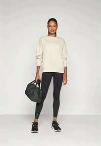 Sudadera crema, leggings negros y zapatos deportivos negros. Sosteniendo un bolso de deporte negro. Diseño simple, forma ajustada y acentos mínimos.