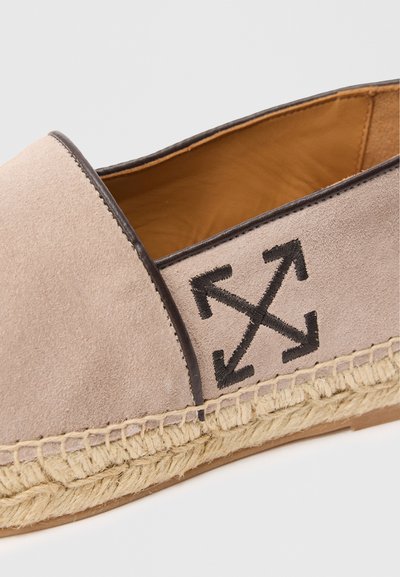 Bežiniai suediniai espadriilai su rudos odos apdaila ir nendrių padais, ant šono turintys juodą siuvinėtą logotipą.