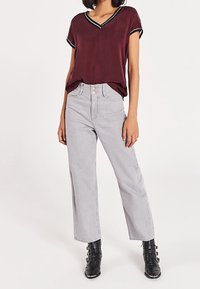 Burgundy short-sleeve shirt with black trim, paired with high-waisted gray wide-leg jeans and black ankle boots with buckles.